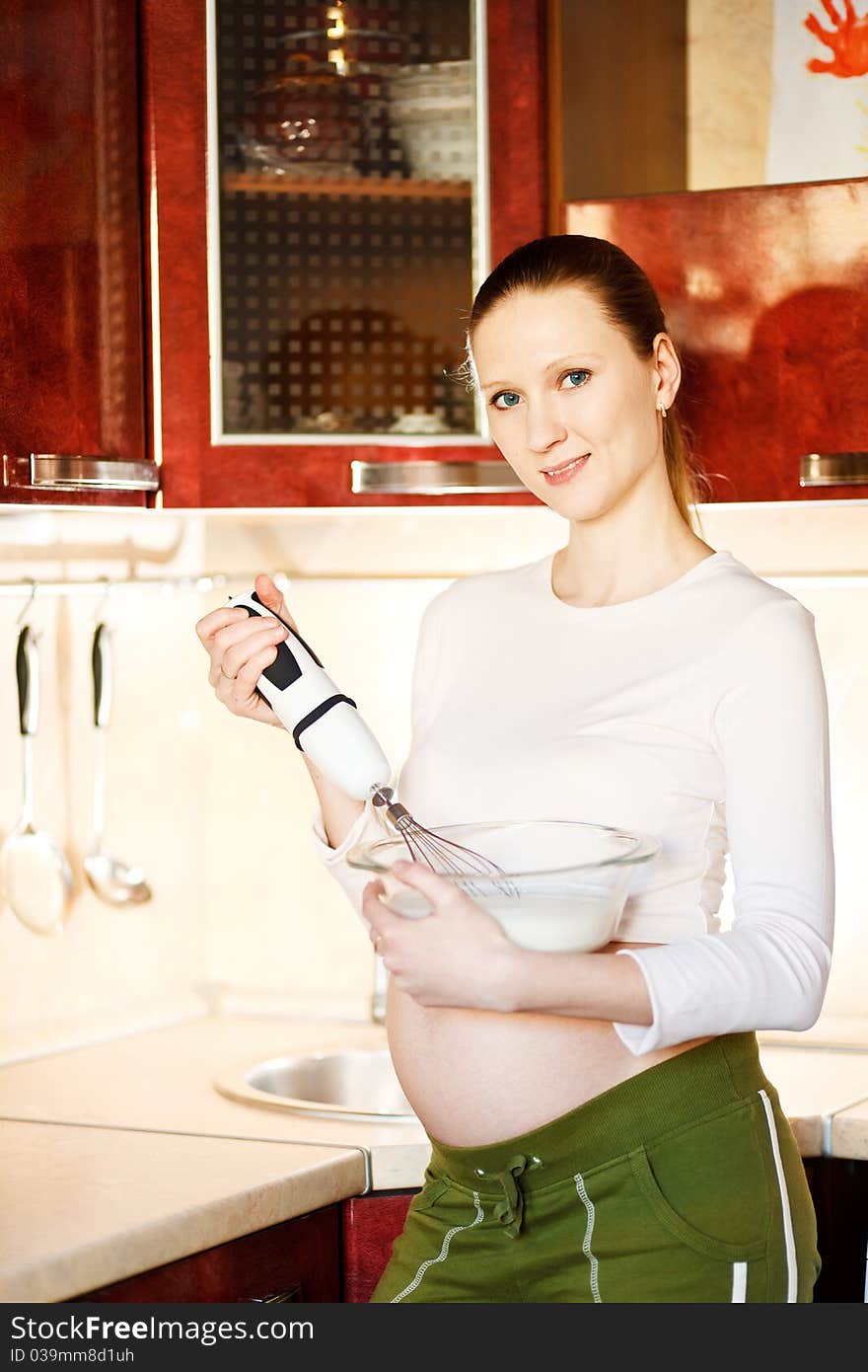 Pregnant woman in kitchen making a food and smilin