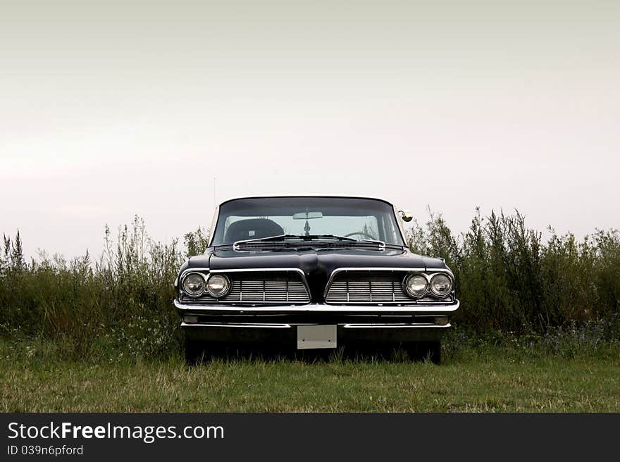 A black american 1960s car parked in a field. A black american 1960s car parked in a field