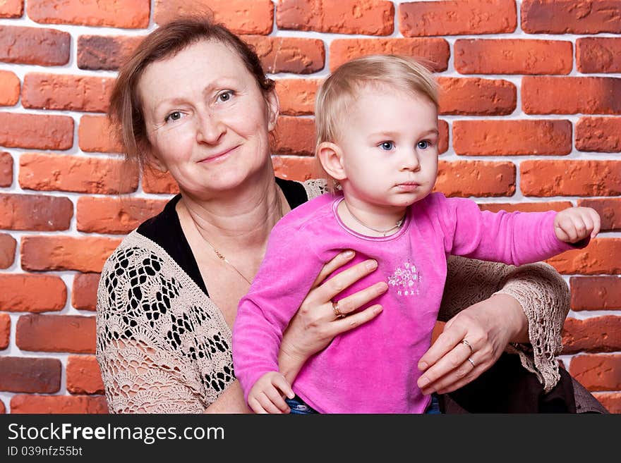 Grandmother kissing her grand daughter against brick wall. Grandmother kissing her grand daughter against brick wall