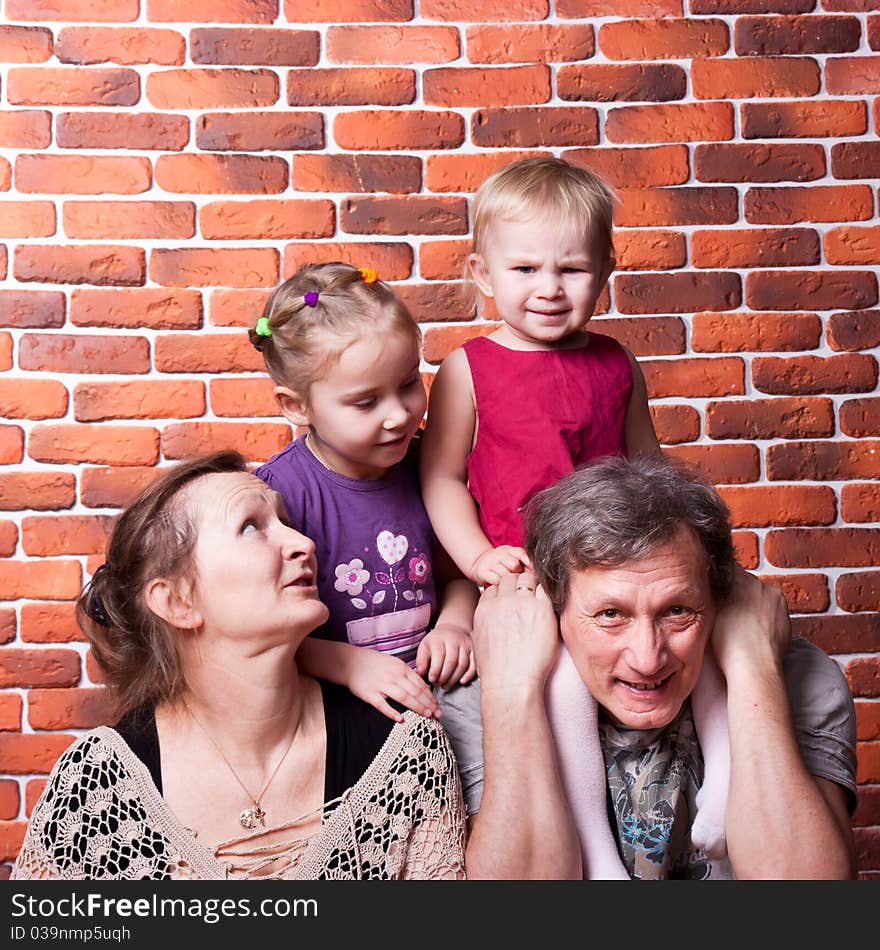 Happy seniors couple with grandchildren against brick wall