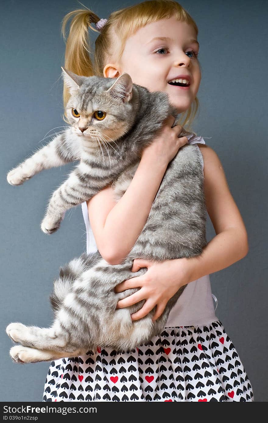 A girl with blond hair is holding a cat and laughs. A girl with blond hair is holding a cat and laughs