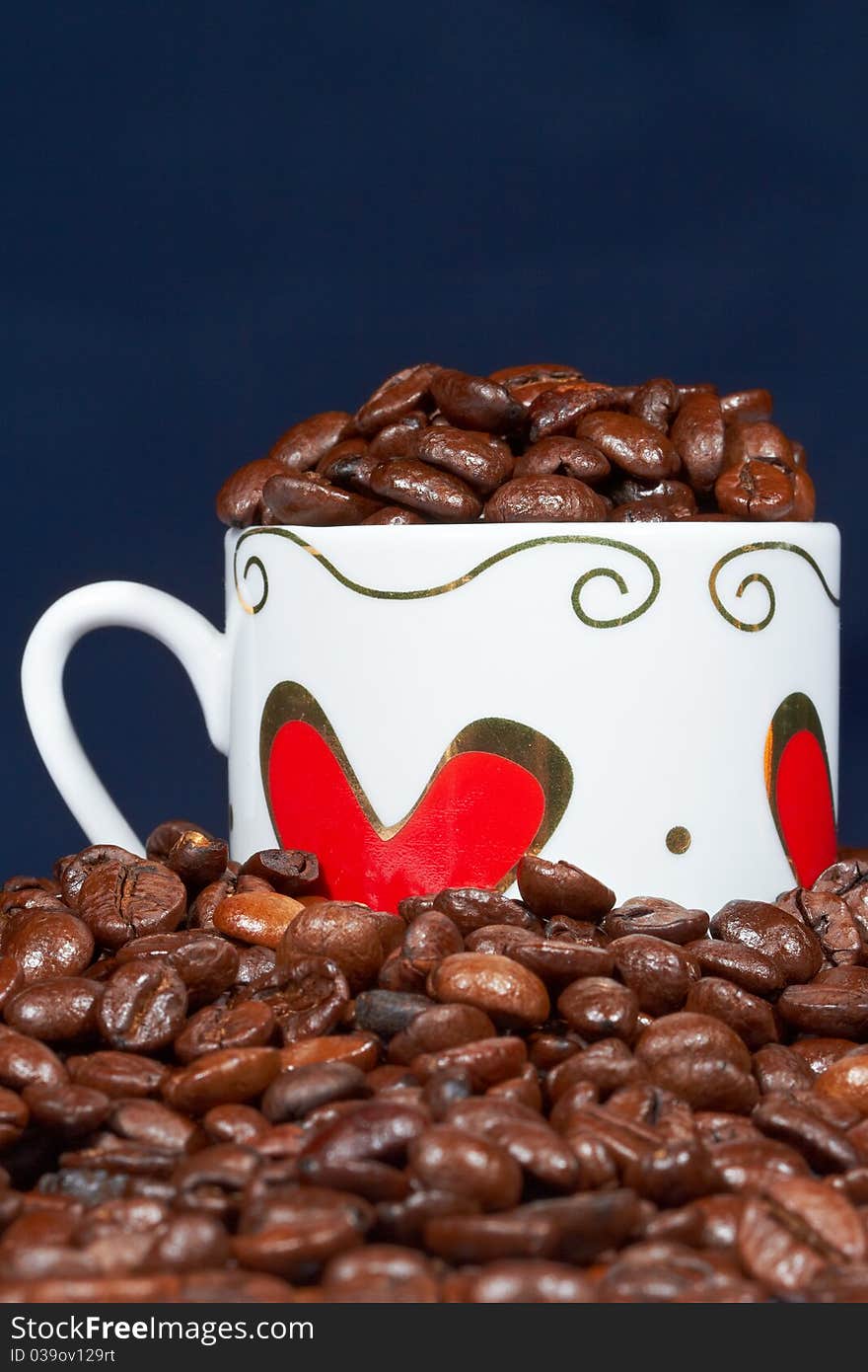 White cup with hearts stands sprinkle on the table beans roasted coffee. White cup with hearts stands sprinkle on the table beans roasted coffee.