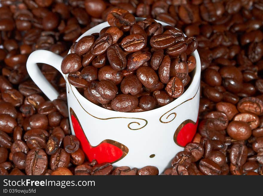 White cup with hearts stands sprinkle on the table beans roasted coffee. White cup with hearts stands sprinkle on the table beans roasted coffee.