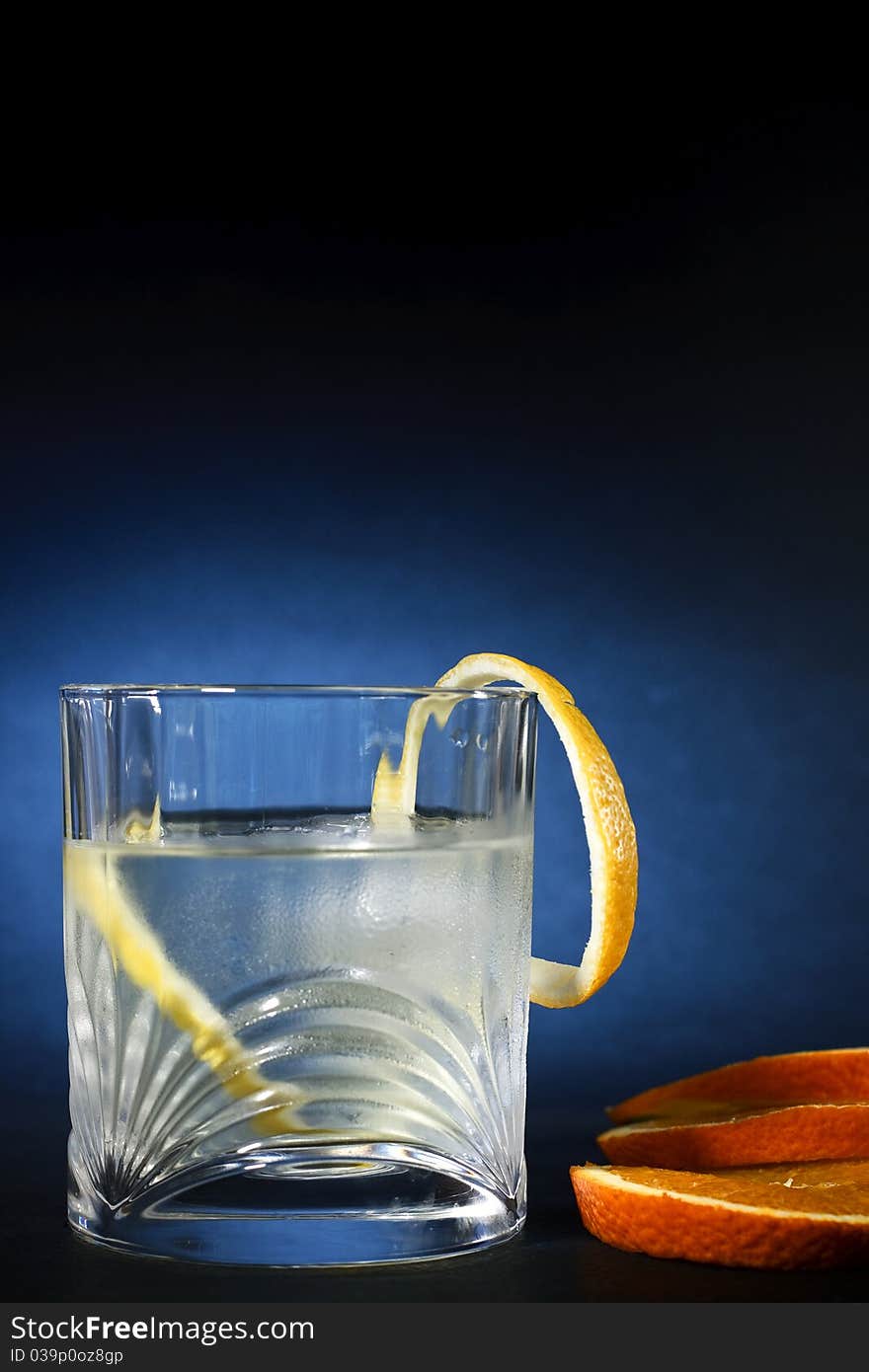 Cold vodka in a glass, with decor oranges and lemon, in black blue background, part of art beverage background. Cold vodka in a glass, with decor oranges and lemon, in black blue background, part of art beverage background