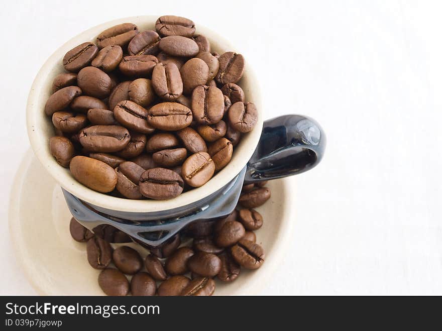 Grain, black coffee sprinkled in small coffee cup with saucer, taken pictures close-up several overhand, on background light fabrics. Grain, black coffee sprinkled in small coffee cup with saucer, taken pictures close-up several overhand, on background light fabrics.