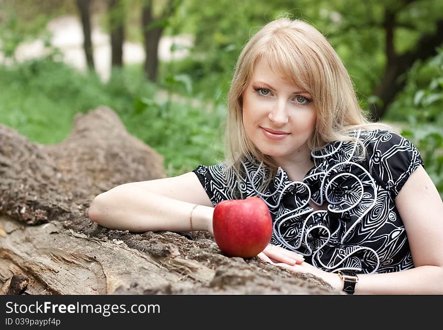 Beautiful smiling young woman with red apple in her hand outdoors, spring day