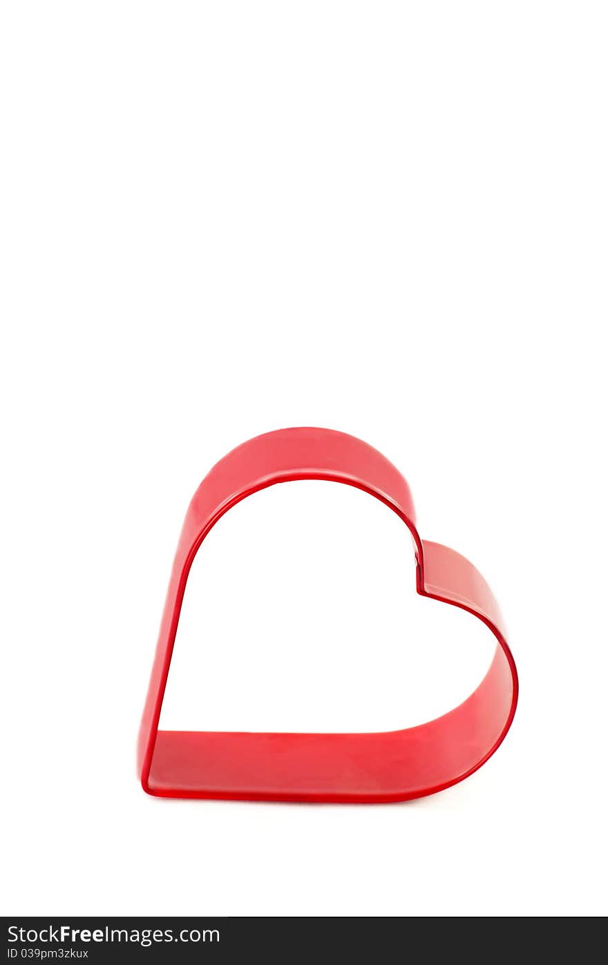 A metal red heart cookie cutter on a vertical white background with copy space. A metal red heart cookie cutter on a vertical white background with copy space