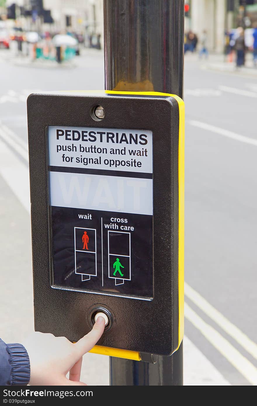 In the foreground, woman's hand presses the button to activate the traffic light. In the foreground, woman's hand presses the button to activate the traffic light