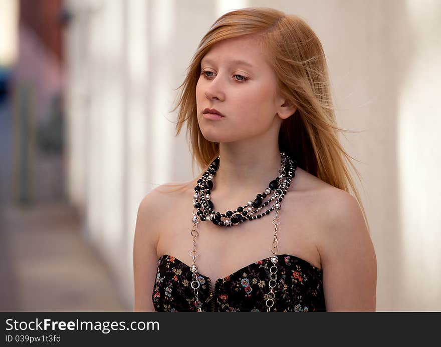 A picture of a lovely blond teenage girl in a lovely tube top and necklaces, standing on sidewalk in a city. A picture of a lovely blond teenage girl in a lovely tube top and necklaces, standing on sidewalk in a city.