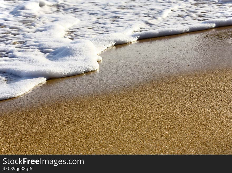 Wet sand on the beach and one wave