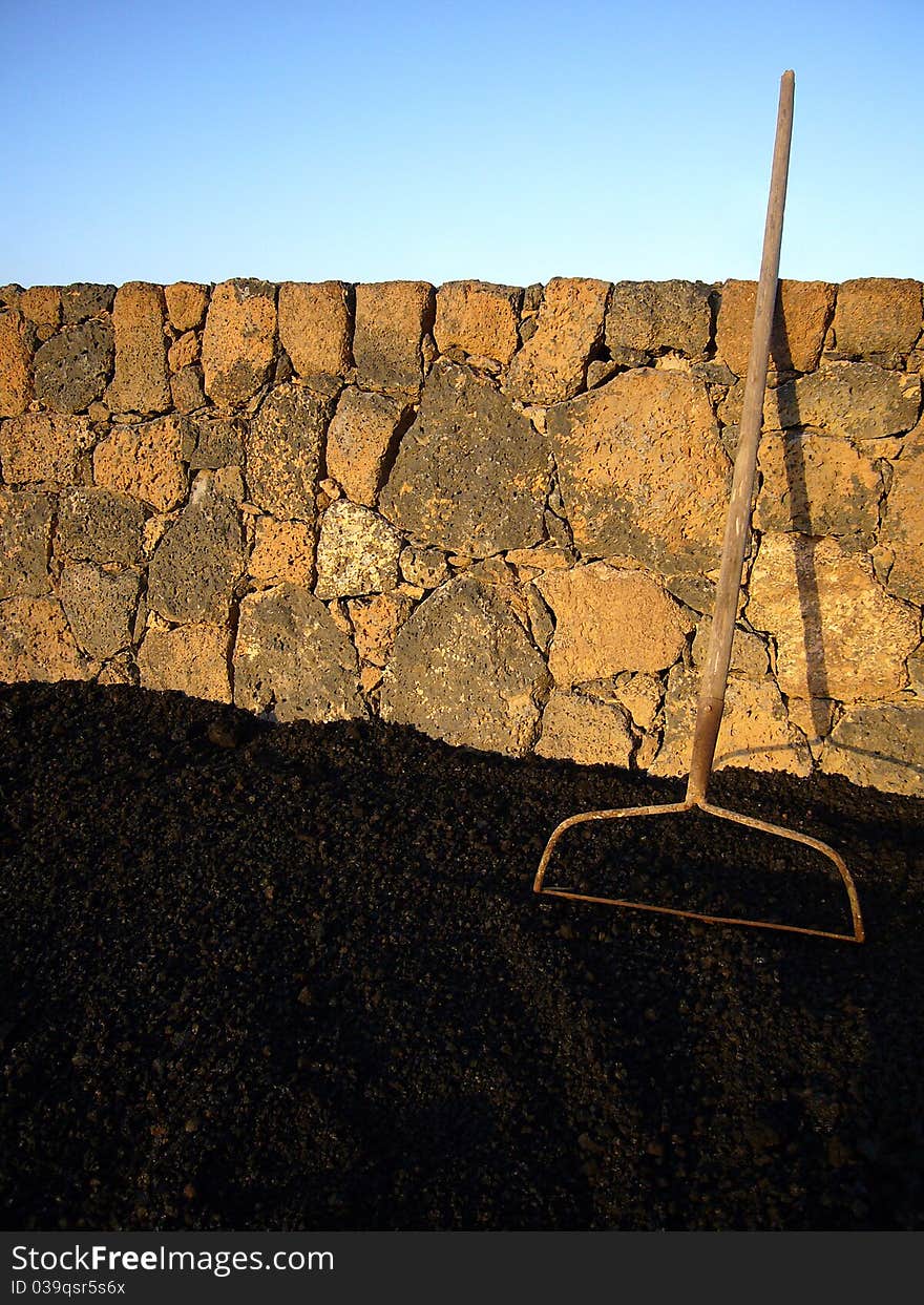 Garden agricultural old rake tool with lava and warm brick wall. Garden agricultural old rake tool with lava and warm brick wall.