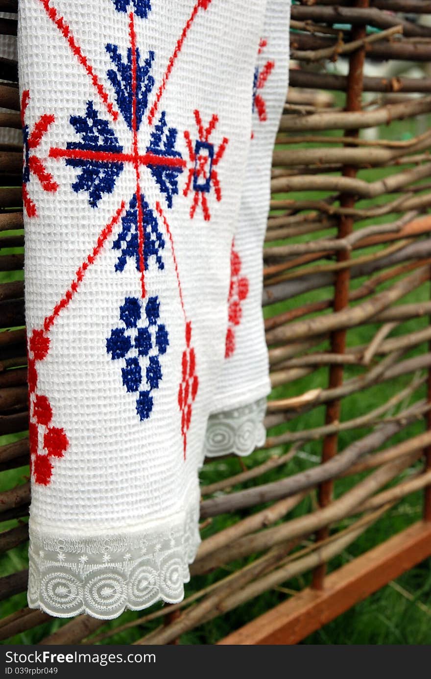 On the fence wooden fence hangs a festive towel. It is embroidered with a cross of red and blue threads in the folk style. On the fence wooden fence hangs a festive towel. It is embroidered with a cross of red and blue threads in the folk style.