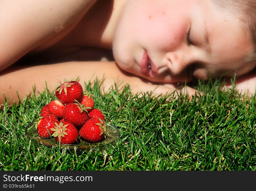 Boy sleeping on grass with pile of ripe strawberries in foreground. Boy sleeping on grass with pile of ripe strawberries in foreground.