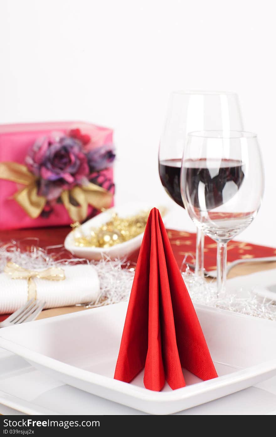 Close-up view of red napkin arranged on white plate, with Christmas present on white background. Close-up view of red napkin arranged on white plate, with Christmas present on white background