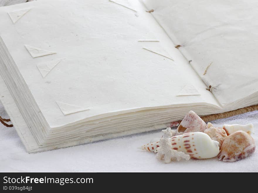 A blank page of a photo album made of recycled paper to paste memories of a day at the seaside or holiday on a towel with seashells in the foreground