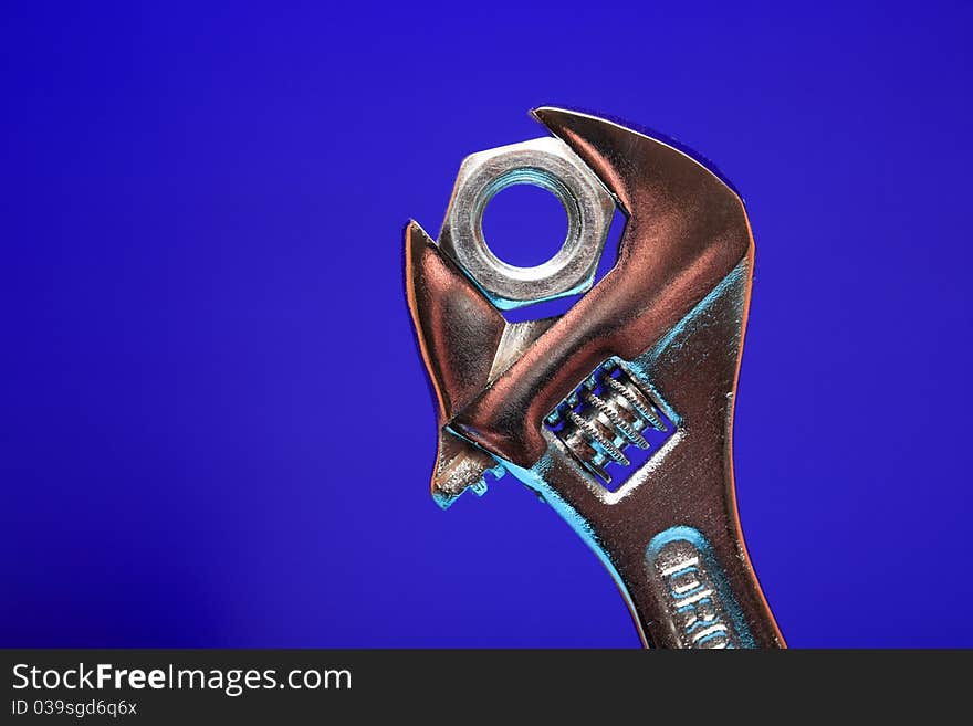 Extreme closeup of adjustable wrench gripping a nut on blue background. Extreme closeup of adjustable wrench gripping a nut on blue background