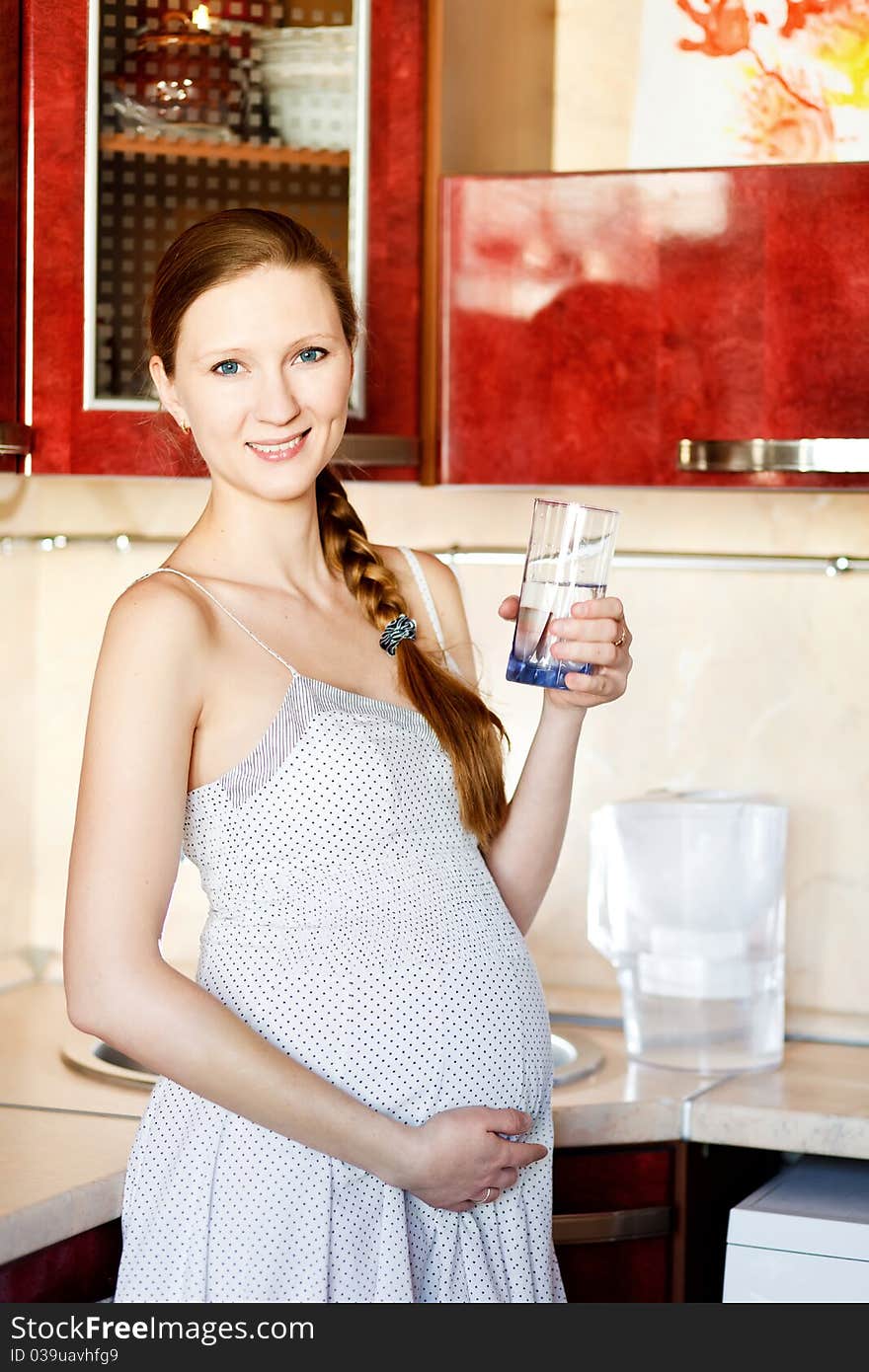 Pregnant woman in kitchen with glass of water smiling