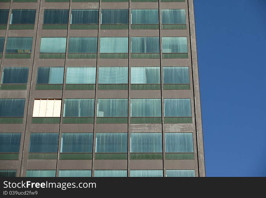 Looking up at a dirty office building with a boarded up missing window. Looking up at a dirty office building with a boarded up missing window