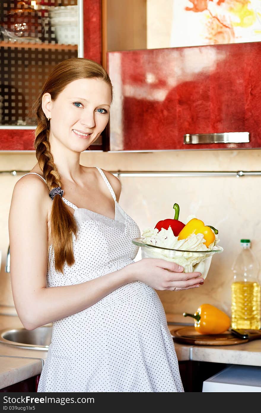 Pregnant woman in kitchen making a salad and smiling