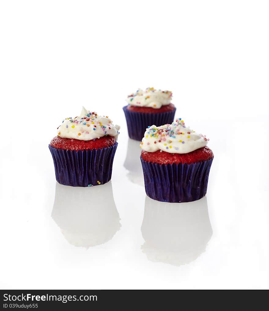 Three mini cupcakes with sprinkles on a white reflective set.