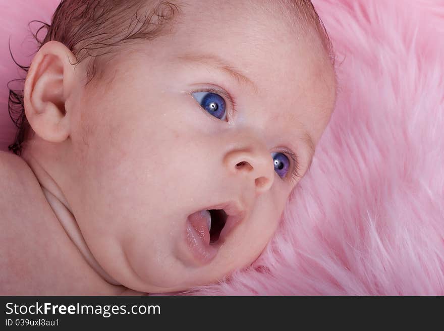 An Adorable Baby With A Pink Background. The baby is wearing purple and has a purple bow in her hair. An Adorable Baby With A Pink Background. The baby is wearing purple and has a purple bow in her hair.