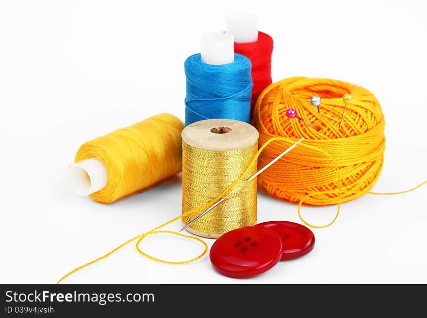 Colored thread, needles and buttons on a white background