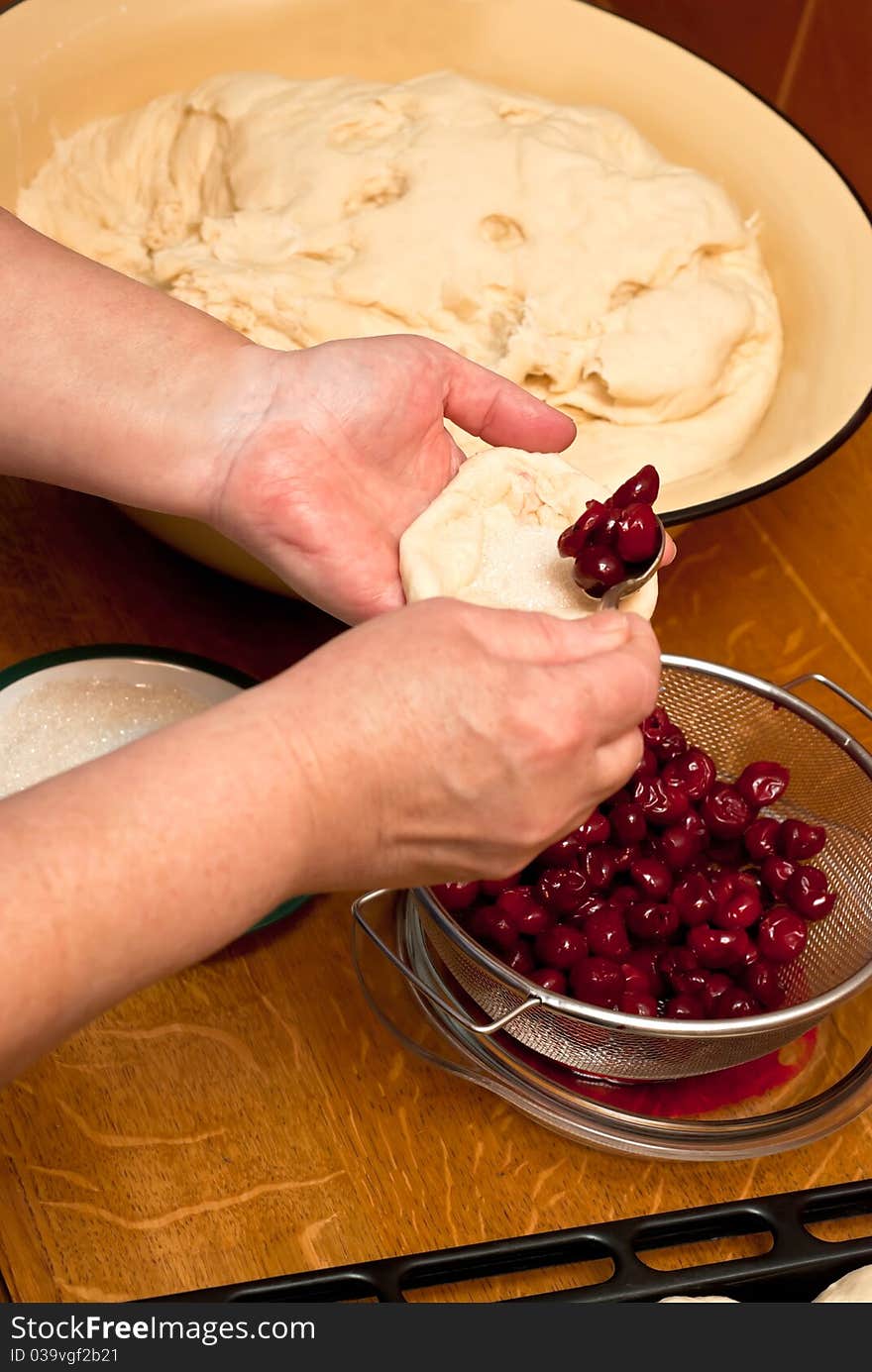 Female hands making small pies with cherry on a table. Female hands making small pies with cherry on a table