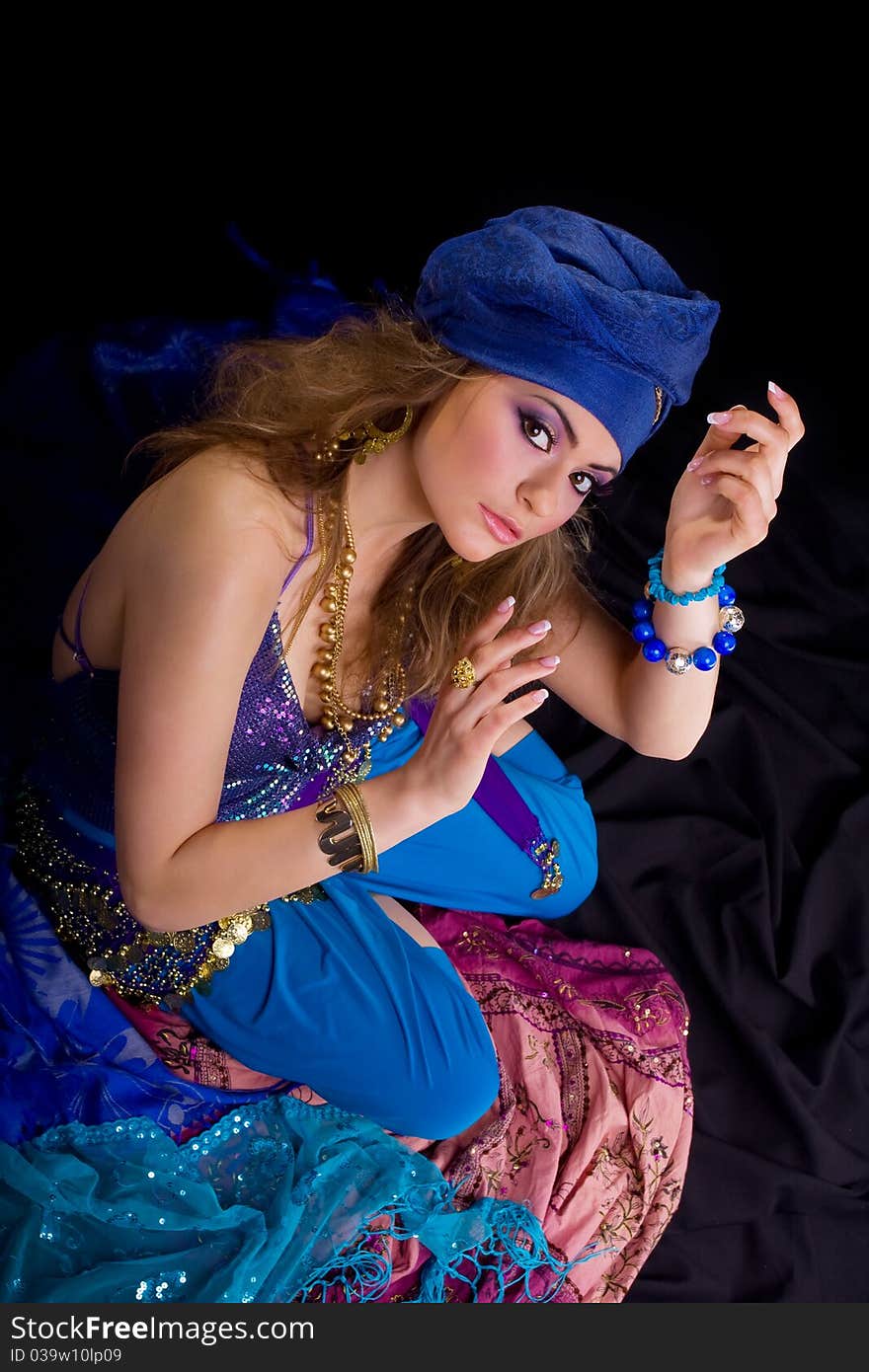 Beautiful girl in a turban and a stylized ethnic costume sits on headscarves