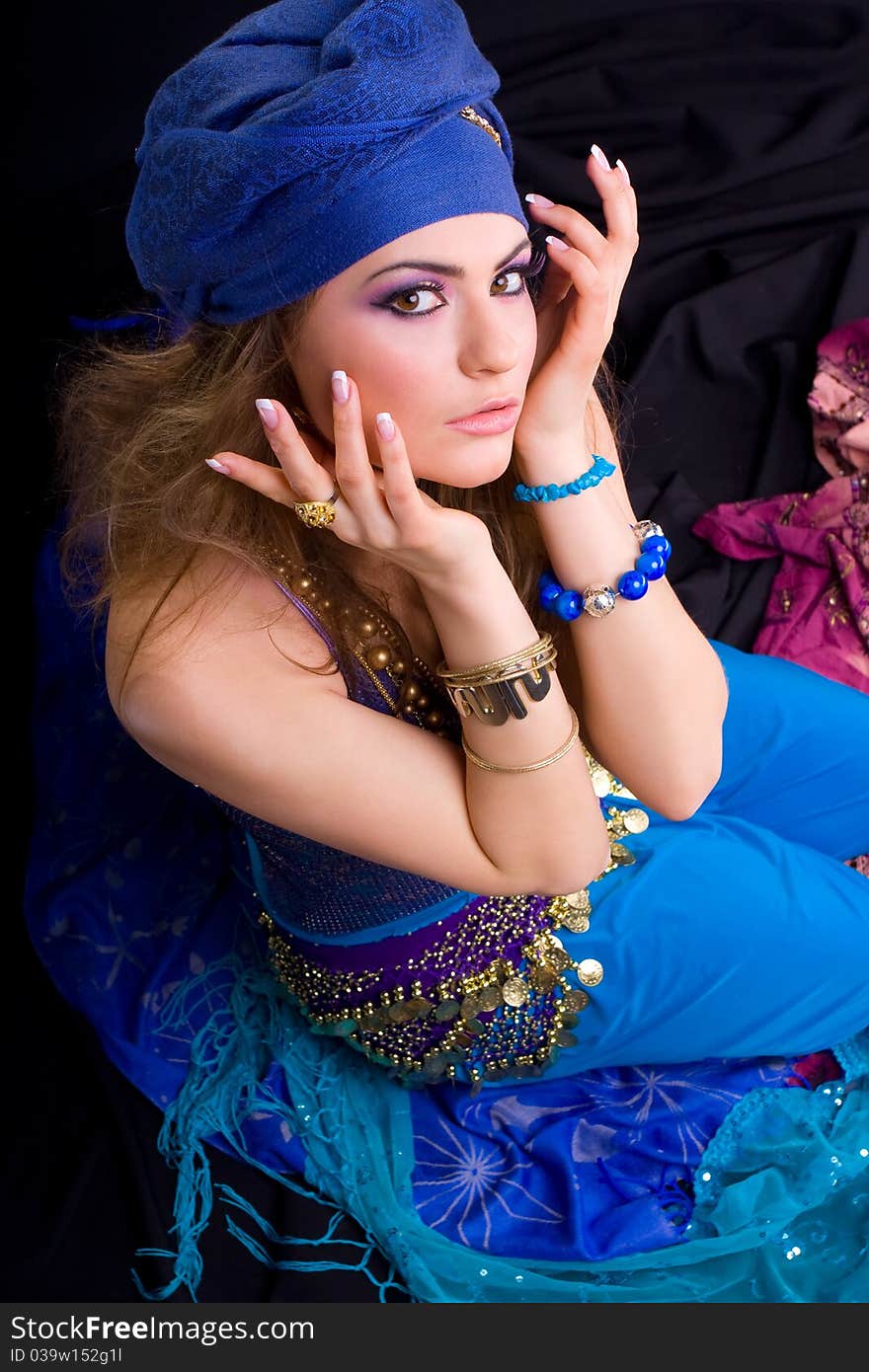 Beautiful girl in a turban and a stylized ethnic costume sits on headscarves