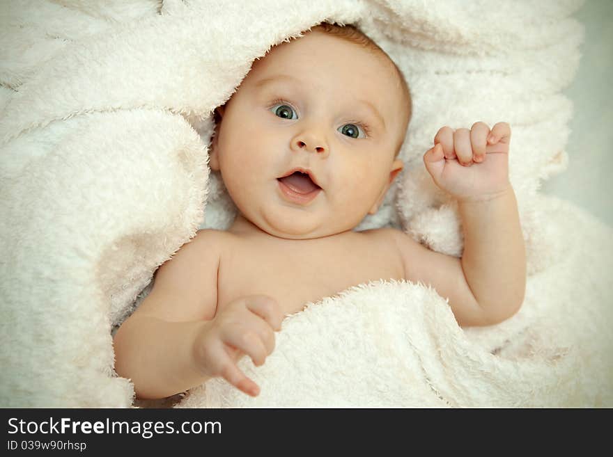 The baby lies in a white towel. He smiles. The baby lies in a white towel. He smiles