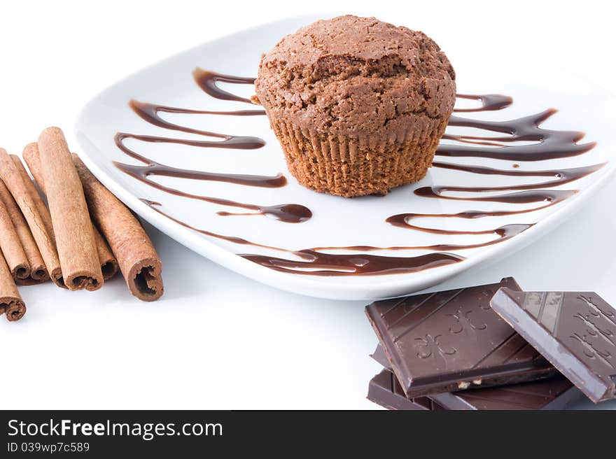 Chocolate muffin on a white plate decorated with chocolate, cinnamon sticks and a chocolate