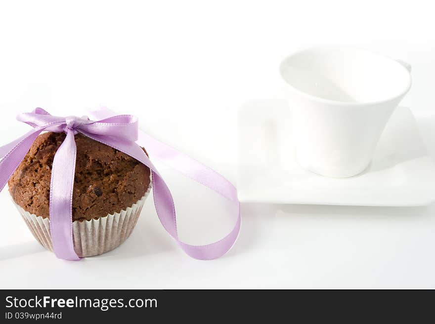 Chocolate muffin, tied with purple ribbon, with a white cup on a white background. Chocolate muffin, tied with purple ribbon, with a white cup on a white background