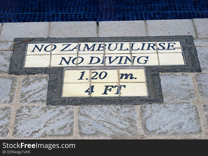 A sign or warning on the edge of a pool in both English and Spanish languages stating there is No Zambullirse and No Diving that the pool depth is 1.2m or 4ft. A sign or warning on the edge of a pool in both English and Spanish languages stating there is No Zambullirse and No Diving that the pool depth is 1.2m or 4ft.