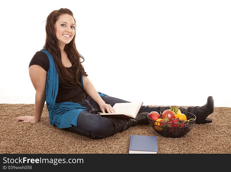 A woman is sitting by some fruit with a book. A woman is sitting by some fruit with a book.