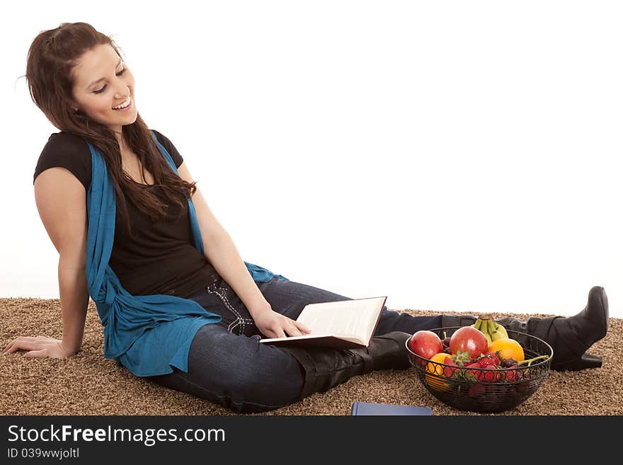 A woman is sitting on the floor reading by some fruit. A woman is sitting on the floor reading by some fruit.