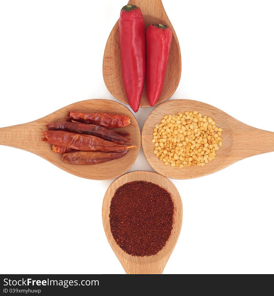 Chili selection of powder, seed and dried in skin and fresh, in four wooden spoons, over white background.