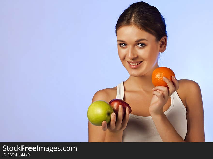 Young beautiful brunette is holding fruit on blue background isolated