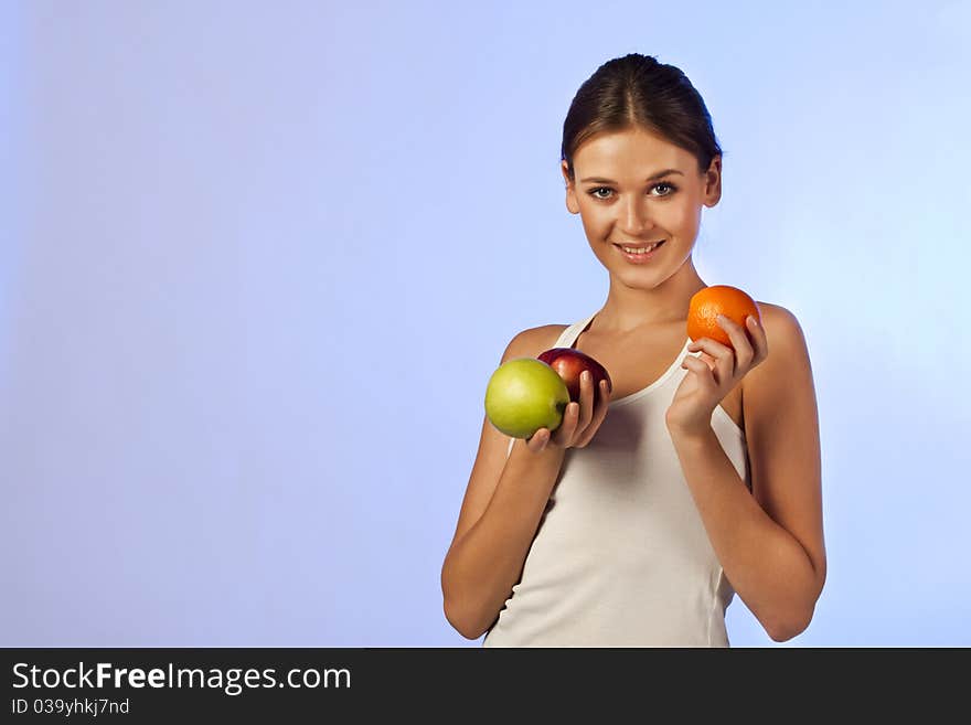 Young beautiful brunette is holding fruit on blue background isolated