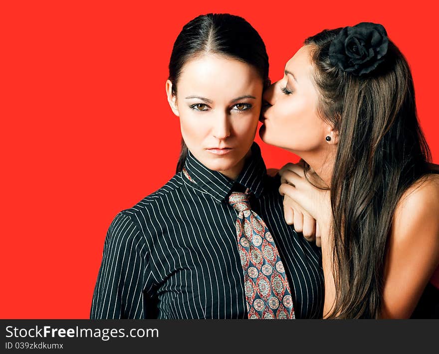 Homosexual women couple, one kissing other on cheek, red background. Homosexual women couple, one kissing other on cheek, red background