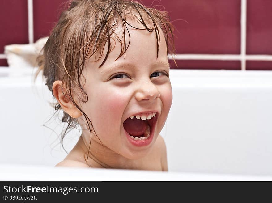 Cute three-year-old girl looking out of a bath and smiling