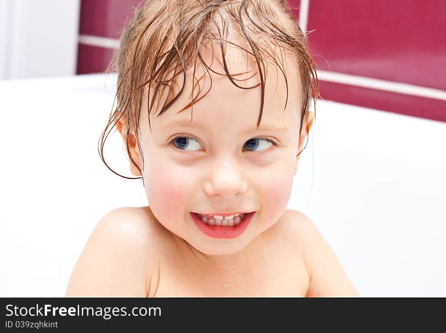 Cute three-year-old girl looking out of a bath and smiling