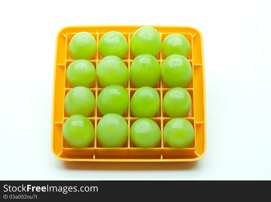 Sixteen green grapes in a square orange plastic holder set against a white background.