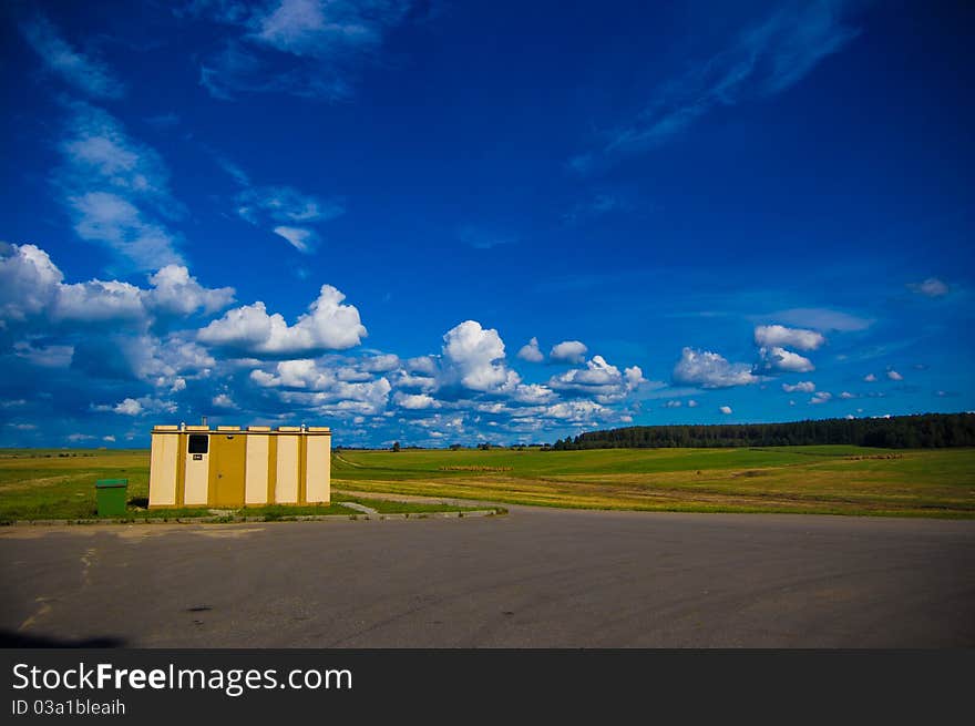 A blue sky with clouds, asphalt, wood away and a roadside stall shower. A blue sky with clouds, asphalt, wood away and a roadside stall shower