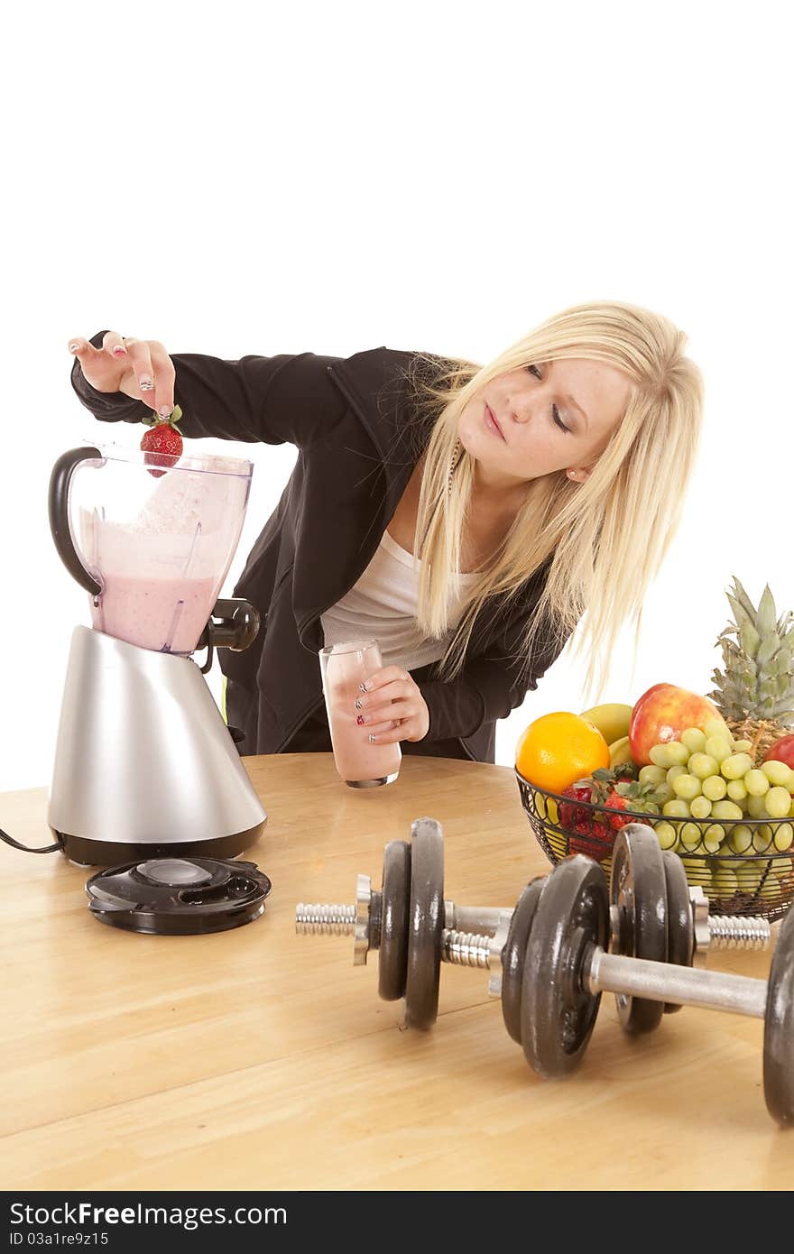 A woman is putting a strawberry into her blender. A woman is putting a strawberry into her blender.