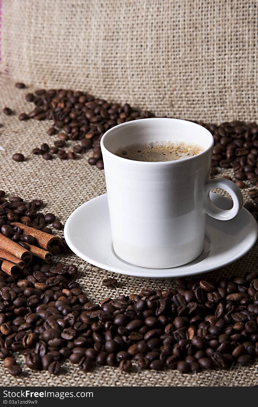 Hot cup of coffee with cinnamon and coffee grains