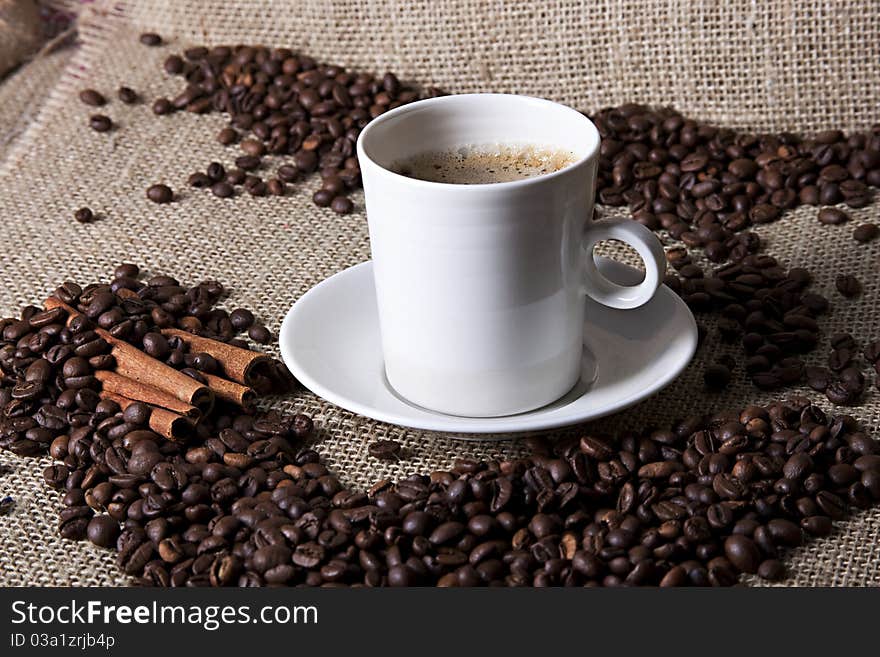 Hot cup of coffee with coffee grains and cinnamon. Hot cup of coffee with coffee grains and cinnamon