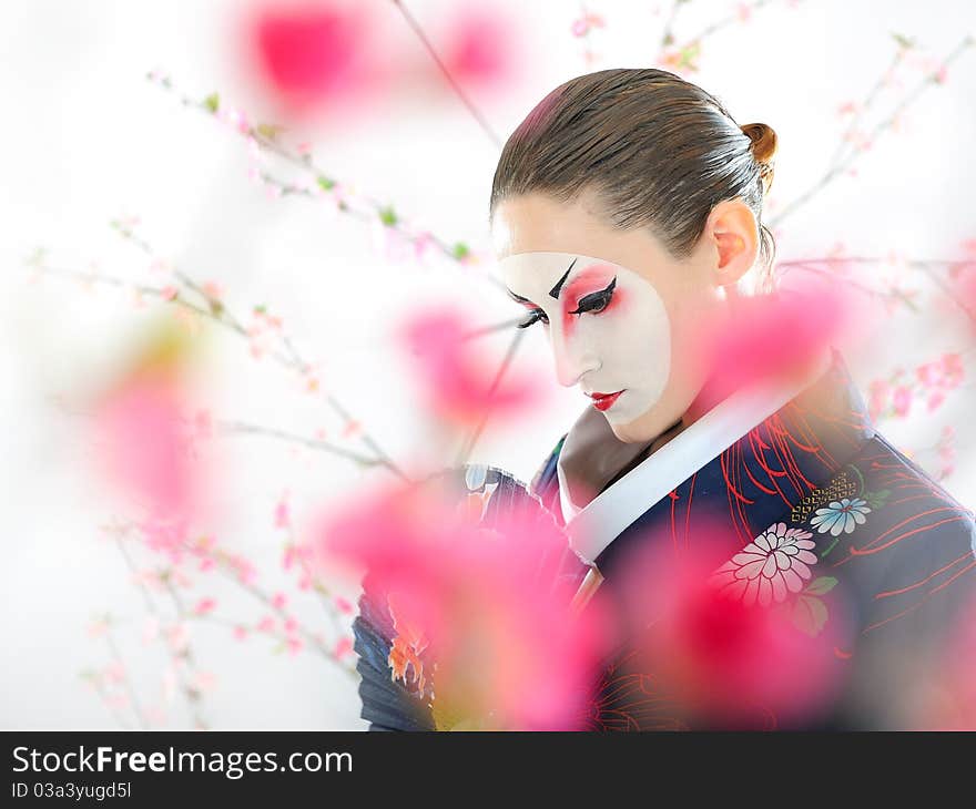 Artistic portrait of japan geisha woman with creative make-up near sakura tree