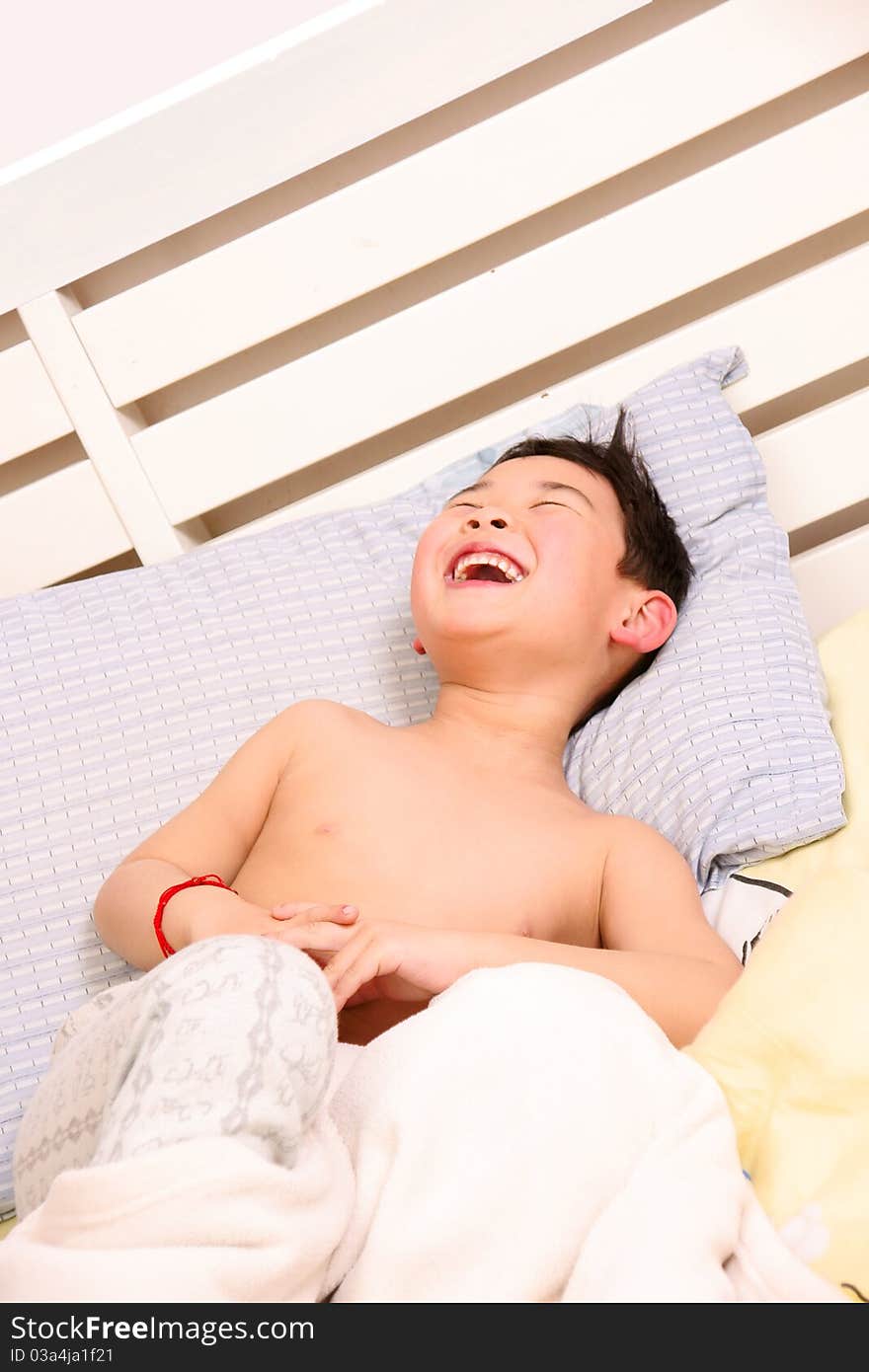 Picture of a little chinese boy laughing happily while lying on the bed. Picture of a little chinese boy laughing happily while lying on the bed