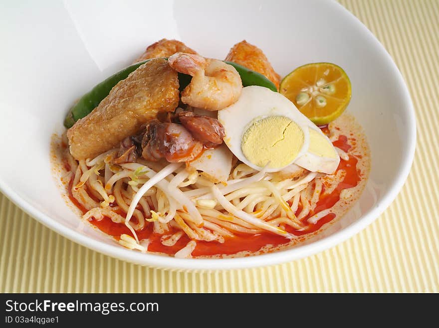 A bowl of curry noodle and garnish with prawn and lime.