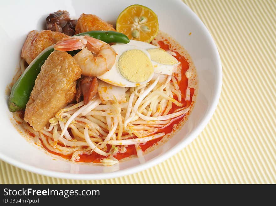 A bowl of curry noodle and garnish with prawn and lime.